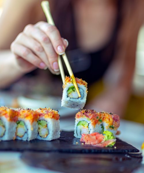 Eating sushi in the restaurant, a woman with a perfect manicure using chopsticks takes a piece of roll, enjoying tasty and healthy food, traditional Asian dish